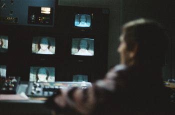 Une silhouette d'homme assis, floue, observe de multiples écrans de contrôle dans le film La mort en direct.