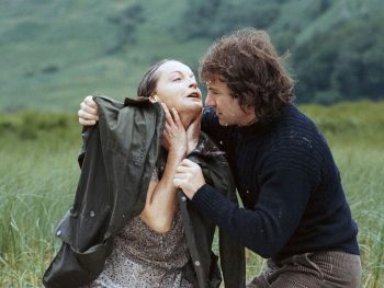 Harvey Keitel réconforte Romy Schneider trempée, perdue au milieu d'une vallée verte, il pose sur ses épaules un manteau ; scène de La mort en direct.