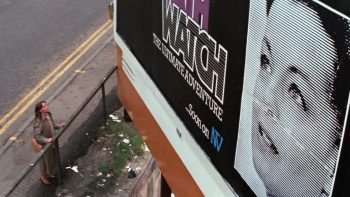 Romy Schneider, toute petite avec l'effet de perspective écrasée de la plongée et du cadrage, observe une gigantesque publicité à son visage, dans le film La mort en direct.