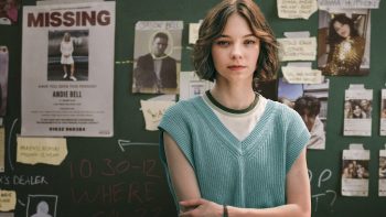 Emma Myers pose les bras croisés devant un tableau avec des affichages sur des disparitions de personne pour la série Meurtre mode d'emploi.