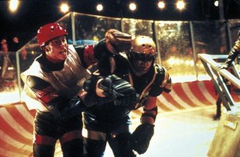 Plan de Rollerball de John McTiernan où deux sportifs jouent du coude vêtus comme des joueurs de hockey avec des éléments de football américain.