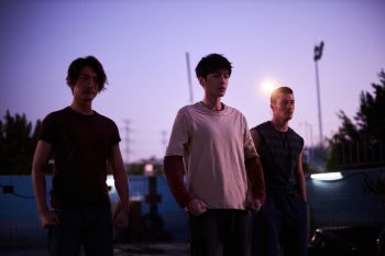 Trois jeunes hommes se baladent dans la rue, sous un ciel de crépuscule violacé ; scène du film Escape From the 21st Century.