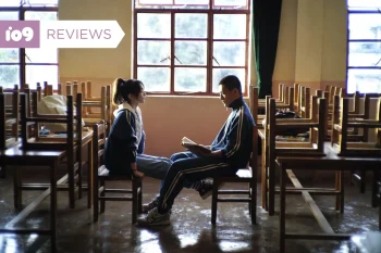 Un jeune homme et une jeune femme assis face à face, dans une salle de classe vide aux chaises retournées sur les tables dans Escape From the 21st Century.