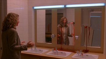 Une femme entre dans une salle de bains dont la glace est brisée, et est tâchée par une ligne de sang ; scène du film Rêves sanglants.