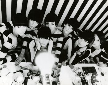 Un groupe de jeune femmes assises dans les loges, avec tout le maquillage sur les tables devant elles ; la loge est couverte d'un papier peint zébré blanc et noir, comme les tenus des filles qui regardent l'objectif ; plan issu du film Qui êtes-vous Polly Magoo ?