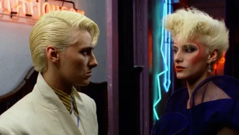 Paula E. Sheppard et Anne Carlisle, blondes peroxydées et looks futuristes des années 80 se regardent dans les couloirs d'un bar aux néons fluo ; scène du film Liquid Sky.