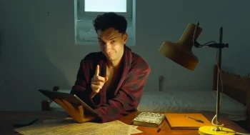 Le narrateur du film, assis dans un bureau de travail éclairé par une petite lampe sur la table, s'adresse à la caméra.