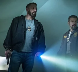 Matt Damon et Ben Affleck, une torche à la main, enquêtent et scrutent dans une pièce aux murs blancs ; scène du film The rip.