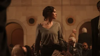 Lily James debout, au milieu d'un public dans ce qui semble être une salle de spectacle, à l'affût, dans le film L'intermédiaire.