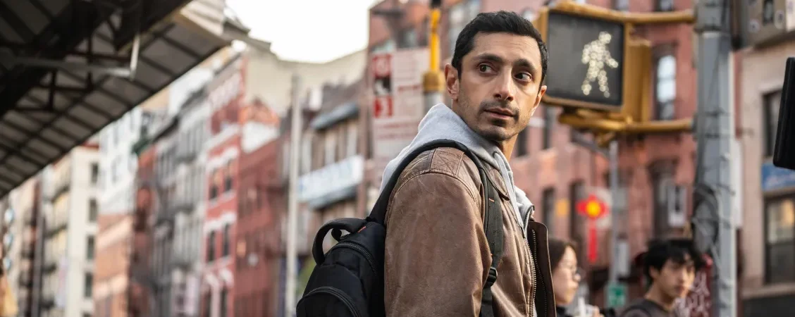 Riz Ahmed méfiant dans une rue bondée, regarde par dessus son épaule ; scène du film L'intermédiaire.