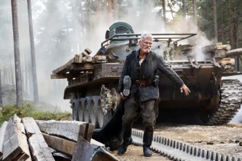 Stephen Lang tire par la jambe un mort à côté d'un tank en pleine forêt dans le film Sisu - le chemin de la vengeance.