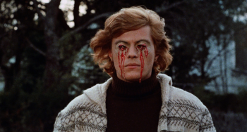 Un homme blond a les orbites ensanglantés ; ses yeux sont absents et du sang coule sur ses deux joues ; il porte un pullover noir et un gilet blanc à motifs ; derrière lui, on devine de la végétation ou un jardin ; plan du film LES CLOCHES DE L'ENFER, projeté à l'Offscreen Film Festival 2026.