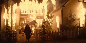 Une silhouette féminine devant une maison en flammes, de nuit, dans Scream 7.