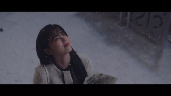 Plan rapproché-poitrine sur Han So-Hee sous une fine neige, regardant le ciel avec un sourire. 