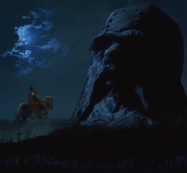 Rouslan, sur son cheval, de nuit, fait face à un immense buste de chevalier, haut de plusieurs mètres, dans le film Rouslan et Ludmila.