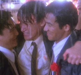 Les trois amis d'Une balle dans la tête, en tenue de mariage, bras dessus bras dessous sous la pluie.