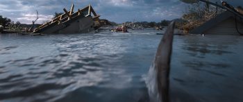 Un aileron de requin fonce vers sa victime dans une eau agitée ; on devine des débris en arrière-plan et le ciel est particulièrement sombre ; plan du film NATURE PREDATRICE de Tommy Wirkola.