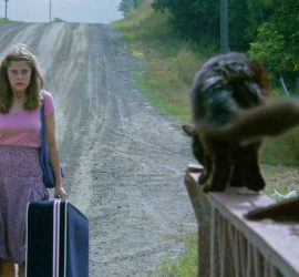 Une femme portant des valises fait face à un chat noir terrifiant