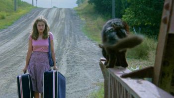 Une femme portant des valises fait face à un chat noir terrifiant 