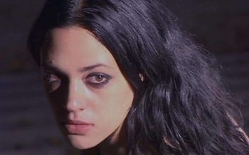 Le visage d'une jeune femme (Asia Argento) en gros plan ; elle regarde la caméra alors que ses yeux sont cerclés de maquillage noir ; ses cheveux sont longs et noirs ; plan du film SCARLET DIVA d'Asia Argento.