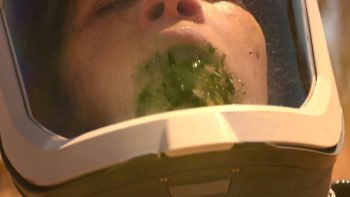 Personnage en gros plan qui vomit une bouillie verdâtre dans son casque.