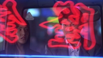 Les personnages de Running out of time de John Woo devant une vitre sur laquelle se reflète des néons rouges d'insignes