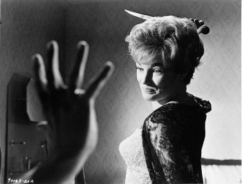 Image en noir et blanc d'une femme avec un couteau qu'elle s'apprête à abaisser sur quelqu'un dont on voit seulement la main droite.
