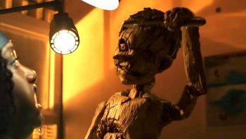 Un pantin de bois maléfique brandit un instrument de dentiste au-dessus du visage d'une femme ; une lumière très jaune est braquée sur la victime ; le pantin affiche un air effroyable et menaçant ; plan du film PINOCCHIO UNSTRUNG, projeté au BIFFF 2026.