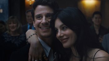 Un homme et une femme sont proches et sourient ; la femme est brune et a le bras droit autour du cou sur l'épaule de l'homme, qui doit être son compagnon ; derrière eux, on devine une assemblée de convives ; plan de la Saison 1 de UN TRES MAUVAIS PRESSENTIMENT, série Netflix.