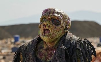 Un affreux humanoïde radioactif ouvre la bouche, ébahi ; son œil gauche est une sorte de pierre noire ; il porte des vêtements usés et sales ; son visage est verdâtre, comme s'il était tombé dans des déchets toxiques ; plan du film THE TOXIC AVENGER UNRATED, projeté au BIFFF 2026. 