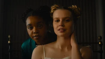 Deux jeunes filles sont filmées en plan rapproché ; l'une est blanche, l'autre congolaise ; la fille blanche tient sa nuque de sa main gauche ; la fille congolaise se trouve dans son dos et appuie son menton sur l'épaule de son amie ; la pièce est sombre, on devine juste des rideaux en arrière plan ; plan du film STEAL AWAY, projeté au BIFFF 2026.