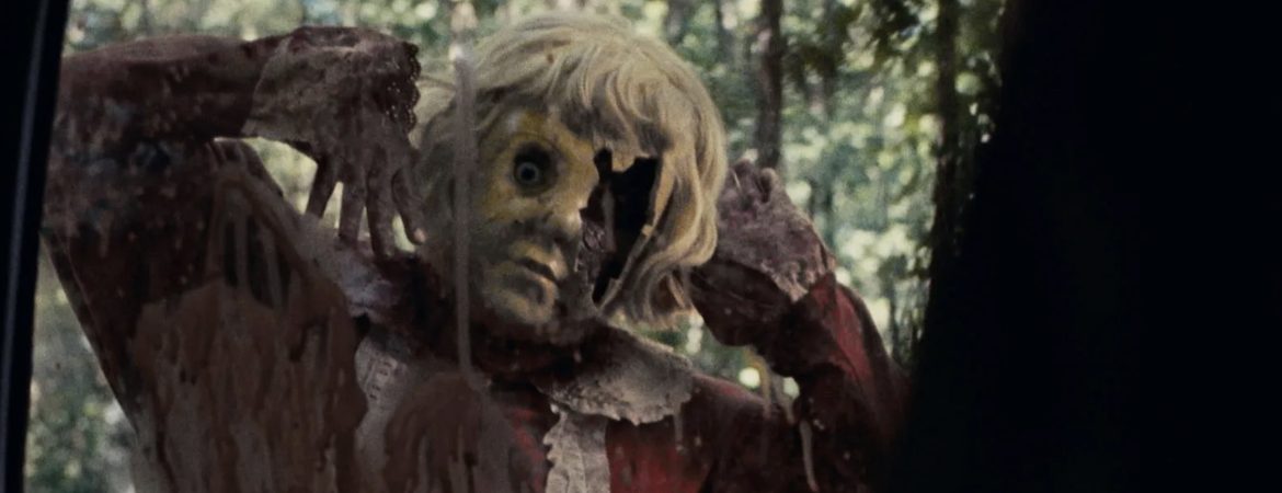 La poupée Dolly dans le film d'horreur du même nom observe sa victime derrière une fenêtre de voiture.