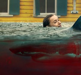 Une jeune femme blonde effrayée se débat dans une eau pleine de sang dans laquelle nage un requin