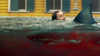Une jeune femme blonde effrayée se débat dans une eau pleine de sang dans laquelle nage un requin ; seul son visage apeuré dépasse de l'eau ; plan du film NATURE PREDATRICE de Tommy Wirkola.
