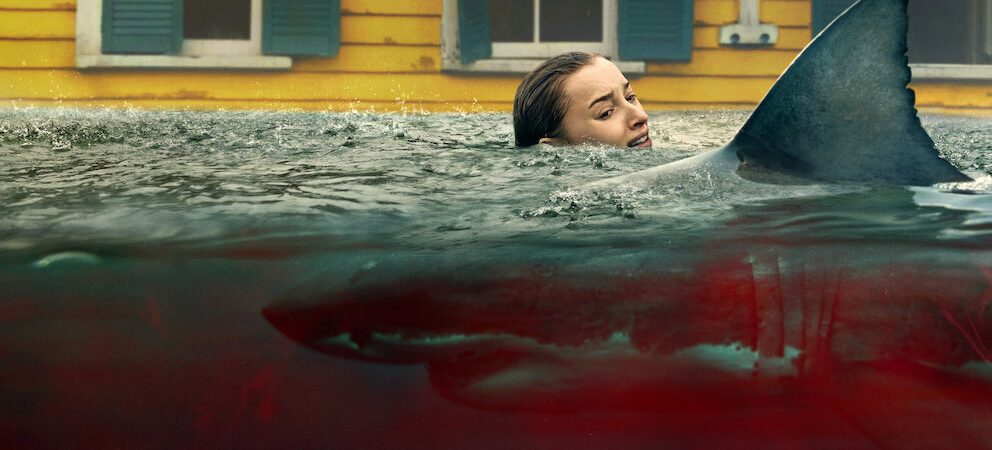 Une jeune femme blonde effrayée se débat dans une eau pleine de sang dans laquelle nage un requin