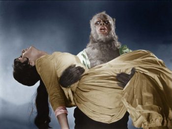 Un loup garou aux poils grils tient dans ses bras une femme brune évanouie portant une grande robe ocre