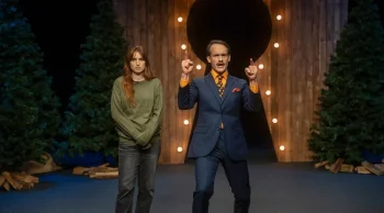 Une femme rousse incarnée par Allison Wheeler se tient prostée à côté d'un présentateur de télévision ringard et fort enjoué