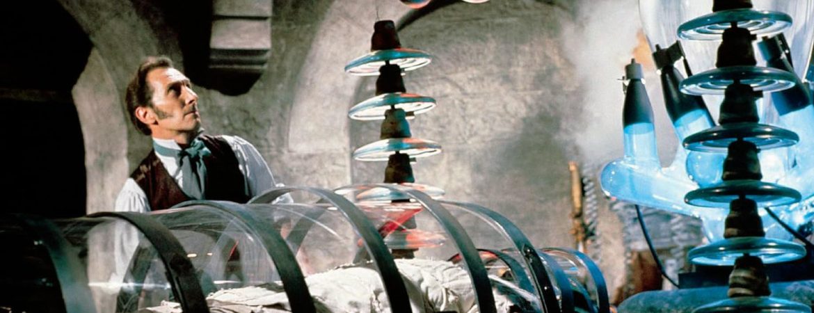 Frankenstein joué par Peter Cushing dans son laboratoire, devant sa créature encore endormie dans une boite en verre, entouré de tubes et d'objets scientifiques.