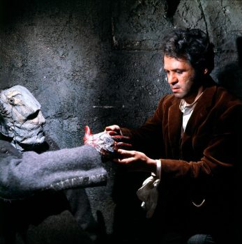 La créature de Frankenstein en train de tendre une main ensanglanté vers Zoltan incarné par Peter Woodthorpe qui lui prend le bout des doigts.