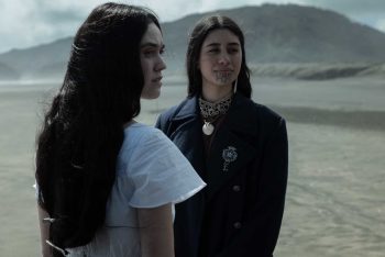 Deux jeunes femmes se font dace dans une étendue désertique ; elles tournent la tête vers la droite de l'image ; celle qui figure a l'avant-plan a de longs cheveux noirs et porte un t-shirt blanc ; l'autre, plus en arrière, doit être maorie ; elle a un tatouage au menton et porte des bijoux traditionnels ; en arrière-plan, une butte s'élève dans le désert ; plan du film MARAMA de Taratoa Stappard.