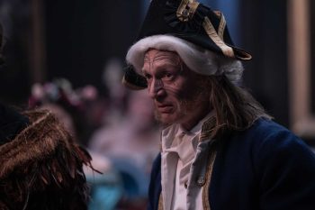 Un homme vêtu de façon victorienne porte une perruque blanche et un chapeau napoléonien ; en avant-plan on devine une épaulette ou un vêtement tribal ; l'homme a le visage tatoué et semble s'apprêter à prendre la parole ; plan du film MARAMA de Taratoa Stappard.