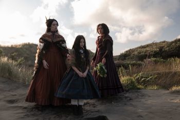 Trois jeunes femmes sont au milieu d'un paysage fait de sable et de végétation basse ; elles sont vêtues d'habits mêlant origine victorienne et traditions maories ; la plus jeune des trois est au centre, les moins jointes ; les deux autres filles, plus âgées, la regardent, tandis qu'elle regarde vers le sable ; dans le ciel, des nuages blancs s'accumulent, malgré une belle luminosité ; plan du film MARAMA de Taratoa Stappard.