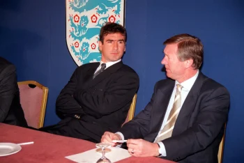 Sir Alex Ferguson dans un costume daté se tient a coté de Eric Cantona en costume, sur une table de conférence de presse à Manchester United