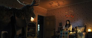 Un élan pénètre dans la chambre d'une enfant et la regarde en amorce du plan ; la petite fille est assise sur son lit, droite, et regarde en direction de l'élan majestueux ; elle porte de longs cheveux ainsi qu'un pyjama ; la chambre est pour partie dans l'ombre, mais une lumière dorée la baigne et les ombres d'un carrousel suspendu au plafond y sont projetées ; la porte de la chambre est grande ouverte ; plan du film DISCLOSURE DAY de Steven Spielberg.