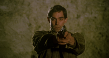 Fabio Testi vise avec son pistolet, cadré en rapproché-poitrine devant un mur de pierre, dans La guerre des gangs.