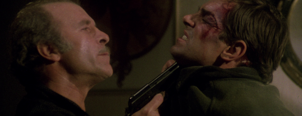 Un gangster tient Fabio Testi par le col, le menaçant avec son revolver, dans le film La guerre des gangs de Lucio Fulci.