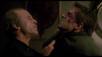 Un gangster tient Fabio Testi par le col, le menaçant avec son revolver, dans le film La guerre des gangs de Lucio Fulci.
