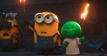 Un Minion en salopette brandit une torche allumée dans une main aux côtés d'une petite créature verte en robe blanche, qui s'apparente à un avatar du Grand Ancien Cthulhu ; la créature verte brandit elle aussi une torche allumée dans une main ; à la droite du plan, on devine la présence d'un second Minion, légèrement en retrait ; la pièce est plongée dans l'obscurité ; sur le mur, en arrière-plan, on aperçoit une large pierre parcourue d'inscriptions ; plan du film DES MINIONS ET DES MONSTRES, de Pierre Coffin.
