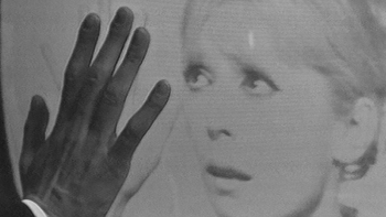 Une main posée sur un écran où est projeté le visage apeuré d'une femme.