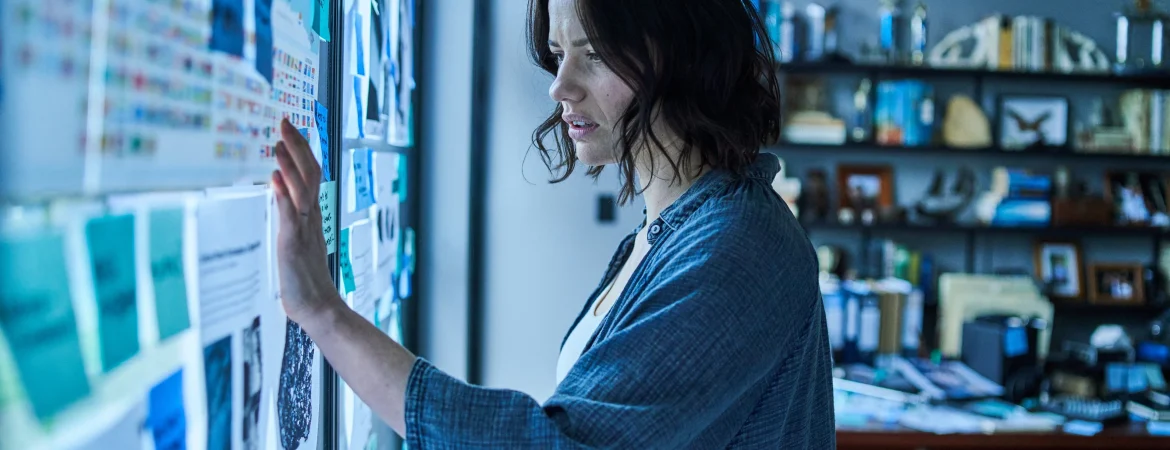 L'héroïne réfléchit sur ses recherches accrochées sur les vitres.